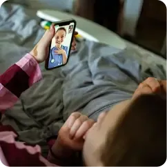 Person lying in bed holding up a phone showing a video call with a vet